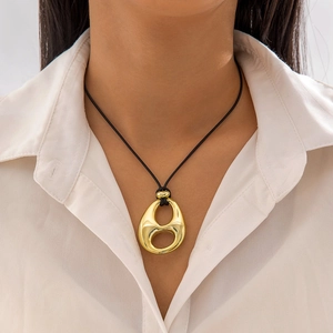 Detalle de un collar con colgante de gota dorada texturizada y cordón trenzado negro