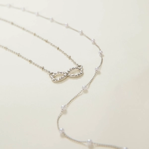 Detail of silver infinity pendant with rhinestones and elegant white pearl chain necklace