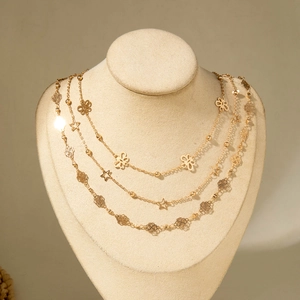 Detailed view of layered gold necklace with star and flower charms on a beige bust