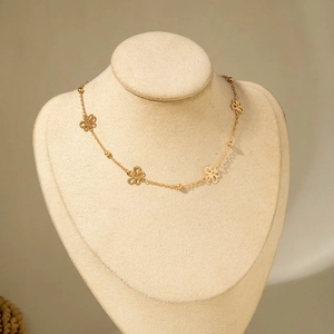 Detail of gold necklace with four hollow butterfly charms on a beige display bust