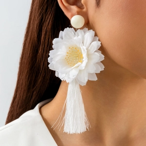 Gros plan de boucles d'oreilles fleurs en tissu blanc avec longues franges sur modèle