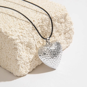 Detalle del colgante de corazón en plata martillada con cordón negro sobre piedra