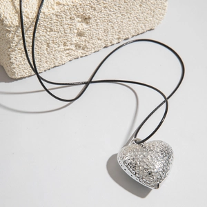 Primer plano de un colgante de corazón plateado martillado con textura en cordón negro