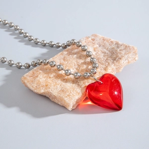 Detalle de colgante de corazón rojo translúcido y cadena de bolas plateada