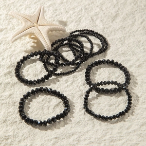 Detail of multi-layer black faceted bead elastic bracelets on a sand textured background