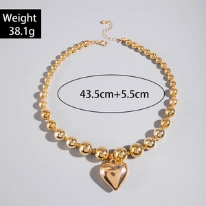 Detalle de collar de cuentas doradas con colgante de corazón grande y cordón de terciopelo