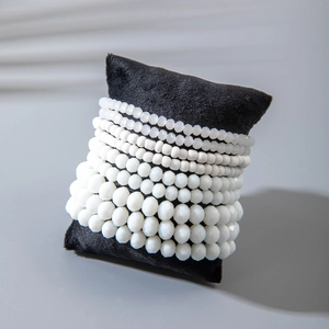 Detail of multi-layer white beaded bracelet set stacked on a black velvet display cushion