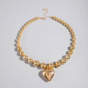 Detalle de collar de bolas doradas con colgante de corazón y cierre de mosquetón ajustable