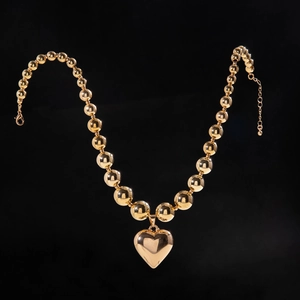 Collar de cuentas doradas con colgante de corazón 3D sobre un elegante fondo negro liso