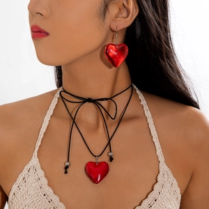 Detail of red heart pendant set with earrings and black cord choker on a female model