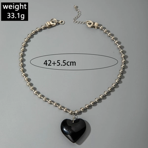 Vista macro del collar de cuentas plateadas con colgante de corazón negro y talla