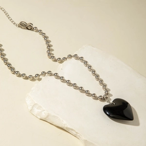 Detalle de un gran colgante de corazón negro en cadena de bolas plateada sobre piedra