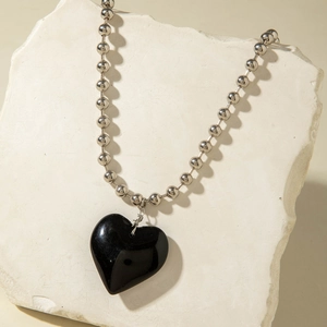 Primer plano de un gran colgante de corazón negro en una cadena de bolas de plata fina