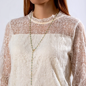 Elegante collar en Y dorado con cuentas turquesas sobre un top de encaje blanco