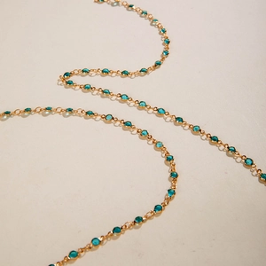 Primer plano de collar en Y dorado con cuentas turquesas sobre superficie con textura