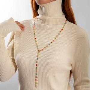 Detalle de collar en Y bañado en oro con cuentas de colores y borlas en suéter blanco