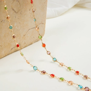 Detalle de collar en Y dorado con gemas multicolores sobre una superficie de piedra