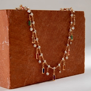 Detalle de collar en Y dorado con gemas coloridas sobre una piedra texturizada