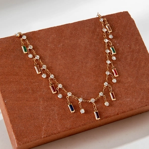 Detalle de collar en Y dorado con gemas de colores vibrantes sobre una base de piedra real