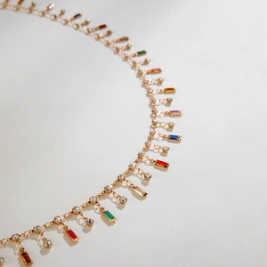 Detalle del collar en Y dorado con gemas rectangulares de colores y diamantes de imitación