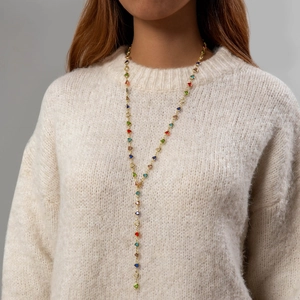 Detalle de collar en Y dorado con cuentas de corazones de colores sobre suéter beige