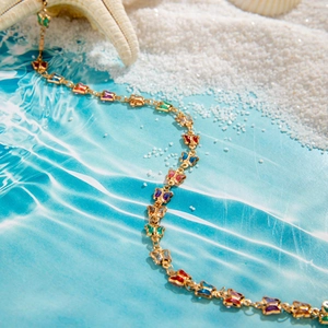 Detalle de collar en Y dorado con mariposas de cristal multicolor en fondo de playa verano