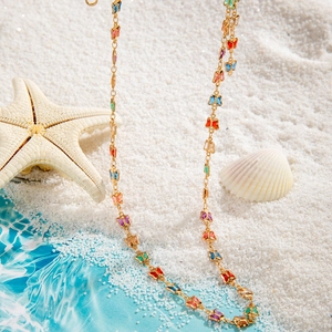 Detalle de dijes de mariposas coloridas en cadena dorada con arena de playa y conchas finas