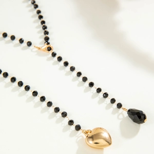 Detail of layered gold necklace with black beads, heart charm and faceted waterdrop pendant