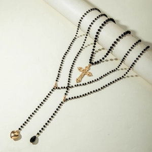 Detail view of multi-layer beaded necklace featuring golden cross and heart pendants