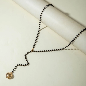 Detailed shot of black beaded Y-shaped necklace featuring a polished gold heart pendant