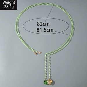 Detailed view of beaded long necklace with gold heart and green teardrop charms