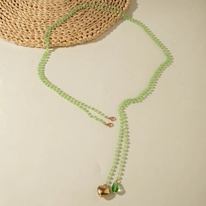 Detail of beaded long necklace featuring a gold heart pendant and green teardrop charm