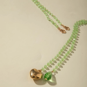 Detail of green beaded necklace featuring a gold heart and emerald teardrop pendant