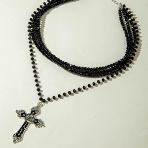 Detail of layered black beaded necklace with vintage silver cross pendant and tassel