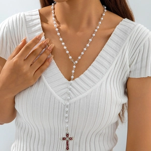Detail of Y-shaped necklace with white pearls and red enamel cross pendant on model