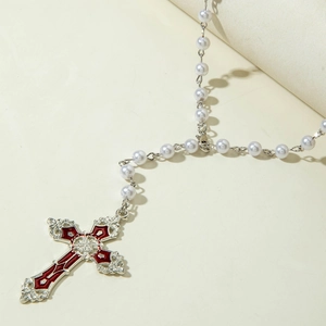 Detailed close-up of vintage silver cross pendant with red enamel and white pearls