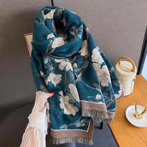 Detail of floral cashmere-like scarf with teal tones and elegant tassels on textured fabric
