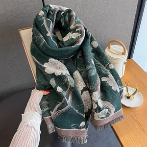 Detail of dark green floral cashmere scarf with tassels held by hand showing thick texture