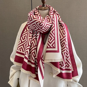 Détail d'une écharpe à motif géométrique rouge et beige avec franges sur un manteau