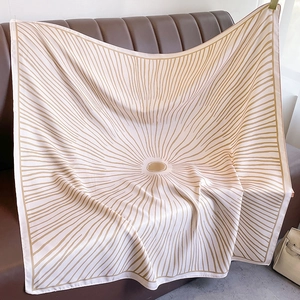 Elegant large silk scarf with golden sunburst geometric pattern on a brown leather sofa