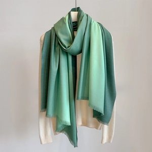 Close-up of green gradient scarf with soft fringe tassels on a white knit sweater