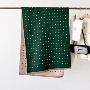 Detail of soft thick scarf featuring heart patterns and fringed edges in dark green and beige