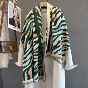 Close-up of green and orange striped knit scarf with fringes on a wool coat