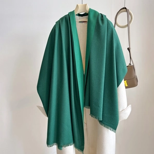 Dark green cashmere-feel scarf with tassels draped over a white wool coat
