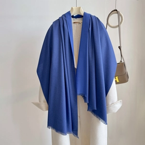 Detail view of royal blue cashmere scarf with fringe on a white coat and tan leather bag