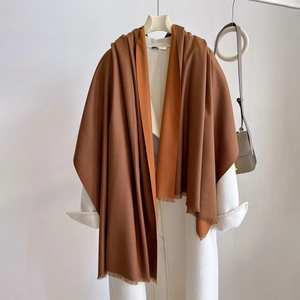 Detail of brown cashmere shawl with delicate fringe tassels against a white coat