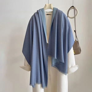 Close-up of double-sided blue cashmere feel scarf with fringe details on white coat
