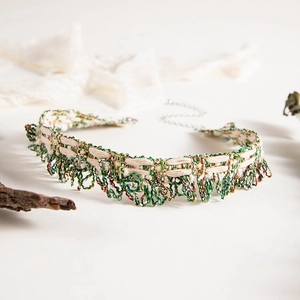 Detailed view of woven lace choker with green and beige silk threads and gold accents