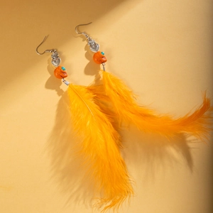 Boucles d'oreilles plumes orange avec crâne et cœur sur fond jaune éclatant