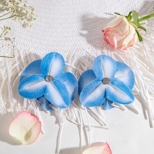 Detail of blue gradient orchid flower hairpins on a white textured fabric with pink roses